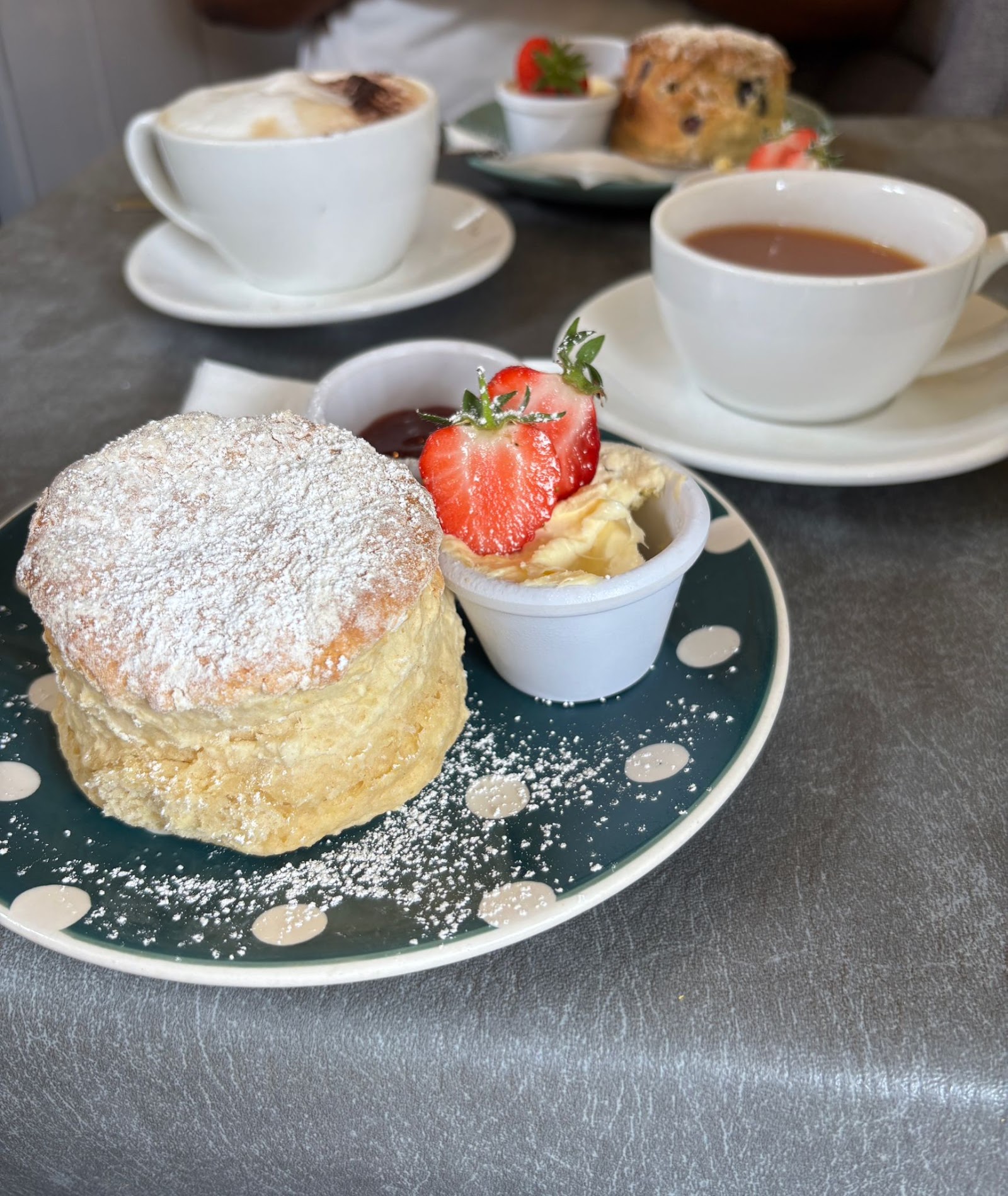 Warm scone dusted with icing sugar, served with coffee
